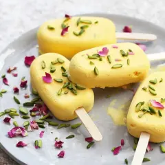 Quatre glaces jaunes, garnies de pistaches et de pétales de rose, sur une assiette. Un délicieux dessert iranien.