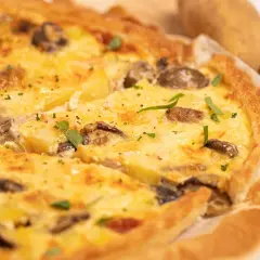 Une délicieuse quiche poulet pomme de terre, garnie de champignons et d'herbes fraîches, prête à être dégustée.
