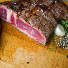 Un succulent bbq côte de boeuf, saignant et parsemé de gros sel, accompagné de romarin frais et d'ail sur une planche en bois.