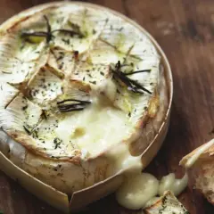 Un camembert au barbecue, fondant et parfumé au romarin, prêt à être dégusté avec une baguette croustillante.