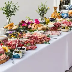 Un buffet généreux avec une présentation soignée : charcuteries, pains, fromages, olives et fleurs. L'étiquette de présentation buffet est respectée.