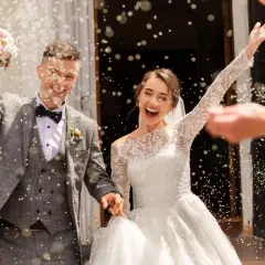 Jeune mariée et marié joyeux sortant de l'église sous une pluie de riz. Idées de mariage pour 20 personnes : une sortie mémorable !