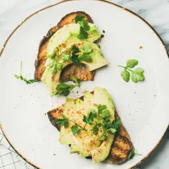 Deux toasts de pain grillé garnis de tranches d'avocat frais, parsemés d'épices et de persil. Une recette avocat simple et savoureuse.