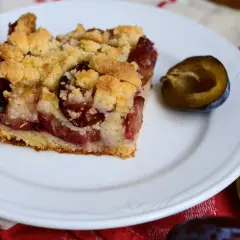Tranche de gâteau aux prunes à la poêle, garnie de crumble doré et de fruits juteux. Une demi-prune à côté.