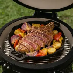Un succulent côte de bœuf au feu de bois, tranché et servi avec des pommes de terre, des oignons rouges et des poivrons dans une poêle en fonte sur un barbecue.