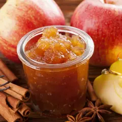 Un pot de confiture de pommes originales, avec des bâtons de cannelle, des étoiles de badiane et des pommes fraîches.