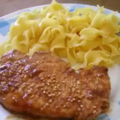 Une côte de porc savoureuse, nappée d'une sauce soja brillante et parsemée de graines de sésame, accompagnée de pâtes fraîches.
