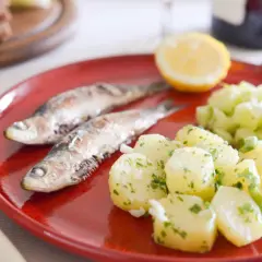 Deux sardines grillées sur une assiette rouge avec une salade de pommes de terre et de concombre. Quel accompagnement avec des sardines grillées !