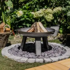 Un brasero en forme de chaudron, prêt à être allumé, avec du bois à côté. Un coin de jardin accueillant pour des soirées conviviales.