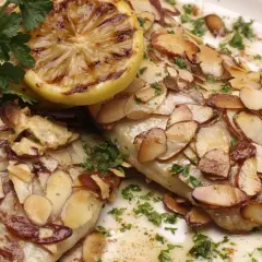 Deux filets de poisson recouverts d'amandes effilées grillées, garni de persil frais et d'une tranche de citron grillée. Un délice de truite aux amandes.
