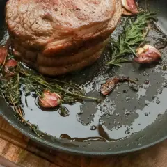 Rouelle de porc au barbecue, dorée et juteuse, mijotant dans une poêle avec de l'ail et des herbes aromatiques.