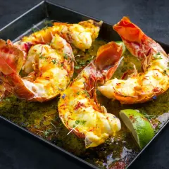 Langoustes grillées sur plancha, nappées d'une sauce verte et garnies de quartiers de citron vert et de thym.