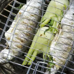 Trois truites au barbecue, garnies d'herbes et de fenouil, grillent sur un barbecue.