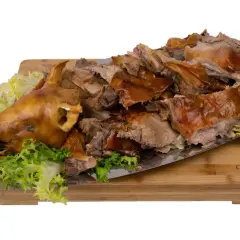 Un cochon de lait entier, rôti à la perfection, est servi sur un plateau avec de la laitue et une rose en tomate. La cuisson du cochon de lait est impressionnante.