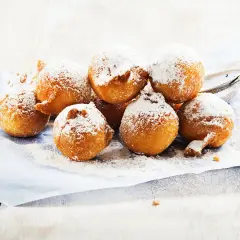 Des beignets dorés saupoudrés de sucre glace, ressemblant à des crottes d'âne, sur du papier bleu.