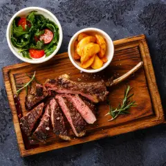 Un succulent accompagnement de côte de bœuf, servi avec une salade fraîche et des pommes de terre rôties sur une planche en bois.