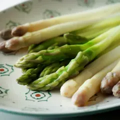 Asperges vertes et blanches sur une assiette décorée, prêtes pour la cuisson.