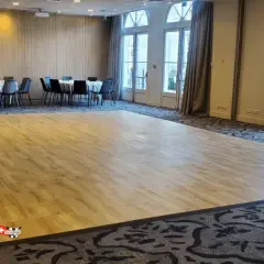 Une piste de danse en bois clair, idéale pour savoir comment faire une piste de danse pas cher. Des tables rondes et des chaises noires sont disposées autour.