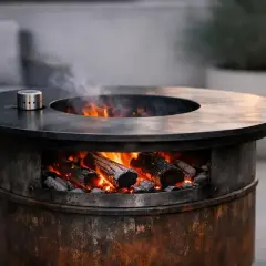Brasero bidon rustique avec des bûches incandescentes et de la fumée s'élevant. Parfait pour une soirée conviviale en extérieur.