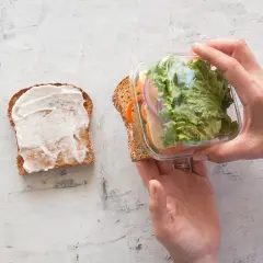 Préparation d'un sandwich crudité : une tranche de pain tartinée de mayonnaise, l'autre garnie de salade, carottes, oignons et fromage, prête à être assemblée.