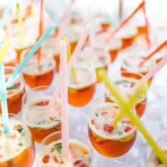 Des verres remplis de cocktails orange vif, garni de fruits et de menthe, avec des pailles colorées. Un parfait cocktail de bienvenue mariage.