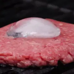 Un steak haché au barbecue, avec un glaçon posé dessus pour une cuisson parfaite.