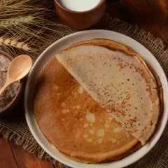Crêpes dorées faites avec de la farine semi-complète, prêtes à être dégustées. À côté, un bol de farine et des épis de blé.
