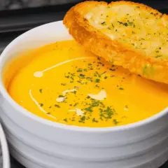 Soupe orange onctueuse, garnie d'herbes et d'un filet de crème, avec une tranche de pain à l'ail. Idéal pour savoir comment épaissir une soupe.