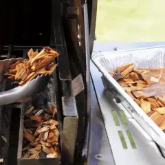 Des copeaux de bois sont placés dans un fumoir pour barbecue Weber. Une autre partie est trempée dans l'eau.