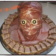 Un plateau de crudités d'Halloween en forme de tête de momie, entouré de petits sandwichs et de charcuterie.