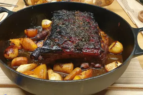 Poitrine de porc au four cuisson lente, dorée et savoureuse, accompagnée de pommes de terre rôties dans un plat en fonte.