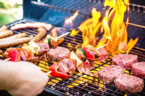 Brochettes et steaks sur un barbecue en feu. La conservation de la viande cuite au barbecue est essentielle pour profiter des restes.