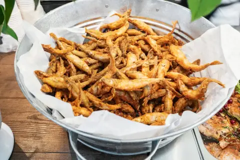 Un seau rempli d'éperlans frits dorés, prêts à être dégustés. Ces petits poissons croustillants sont un délice.