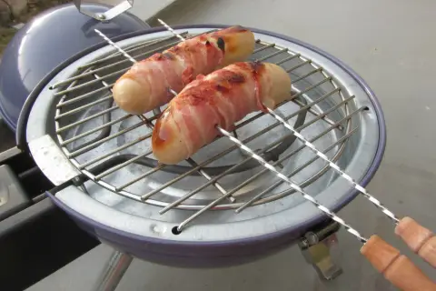 Deux boudins blancs enroulés de lard grillent sur un barbecue. Un délice pour un barbecue estival.