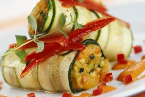 Rouleaux de courgette en lamelle garnis de légumes et de poivrons rouges, décorés d'herbes fraîches.