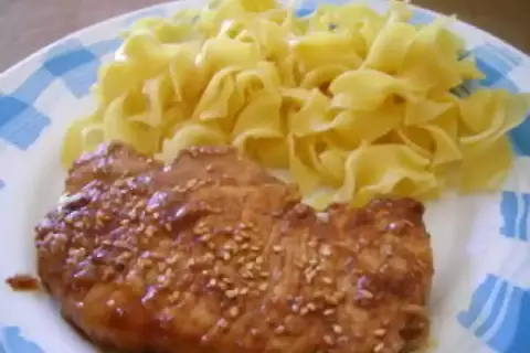 Une côte de porc savoureuse, nappée d'une sauce soja brillante et parsemée de graines de sésame, accompagnée de pâtes fraîches.