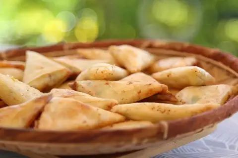 Un panier rempli de samoussas dorés, garniture pomme de terre fromage. Parfait pour un apéritif gourmand en extérieur.