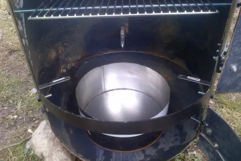 Intérieur d'un fumoir fait maison avec un bidon. Une grille est visible en haut, et un récipient métallique au centre.