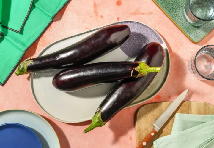 Trois aubergines allongées sur une assiette, prêtes pour des recettes d'été. Ces légumes de juin promettent de délicieux plats.