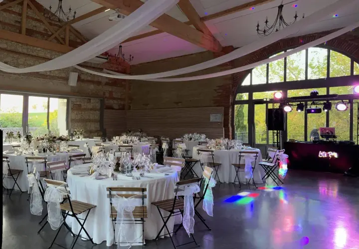 Salle de réception décorée pour un mariage de 80 personnes, tables dressées, lumières d'ambiance et DJ prêt à animer la soirée.