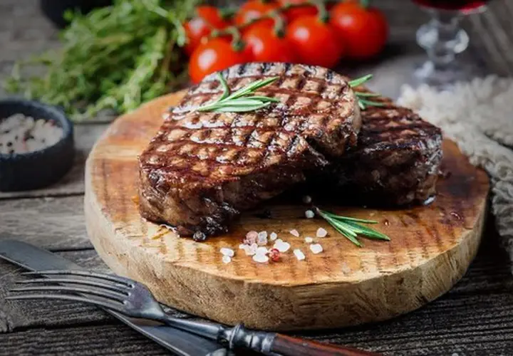Deux steaks grillés sur une planche en bois, parsemés de gros sel rose. Une question se pose : quand saler la viande au barbecue pour un résultat parfait ?