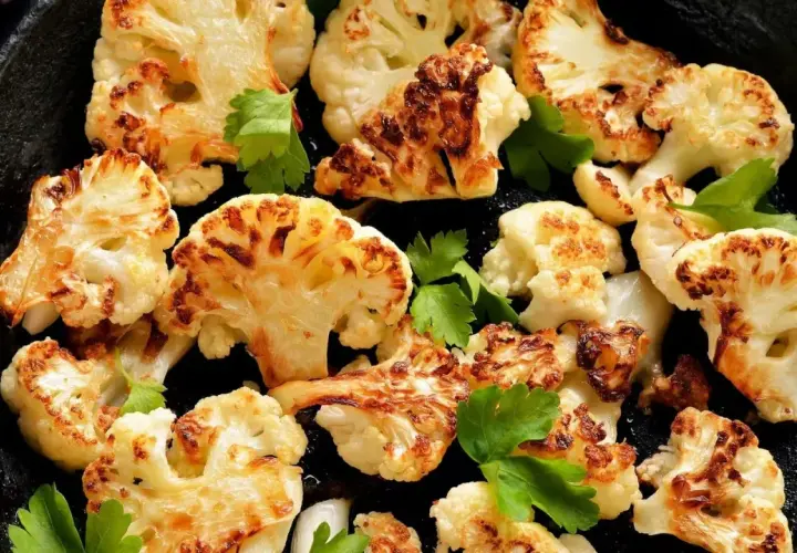 Tranches de chou-fleur rôti au four, dorées et caramélisées, garnies de persil frais dans une poêle en fonte.