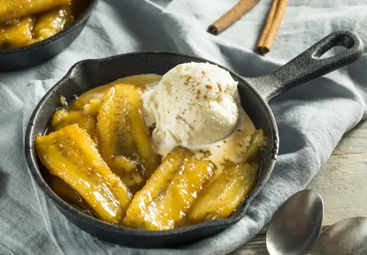 Bananes flambées au barbecue, servies chaudes dans une poêle en fonte avec une boule de glace à la vanille saupoudrée de cannelle.