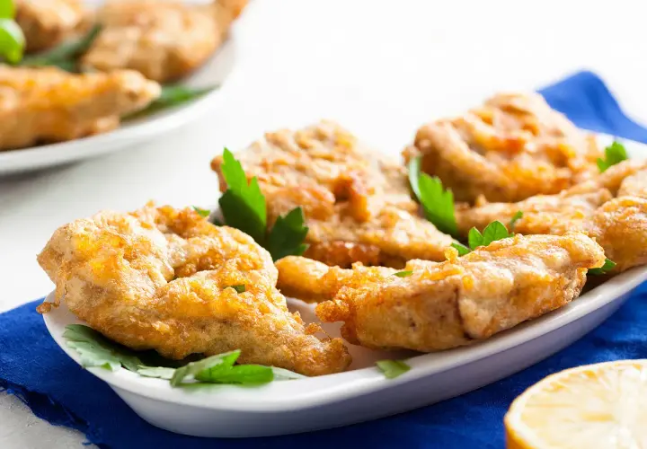 Délicieux artichaut frit, croustillant et doré, servi sur une assiette blanche avec des herbes fraîches et un quartier de citron.