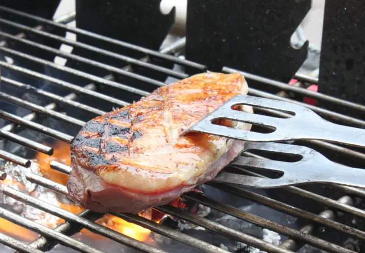 Une aiguillette de canard au barbecue, saisie à la perfection, avec des marques de grill et une peau dorée. Les pinces à barbecue maintiennent la viande sur la grille chaude.