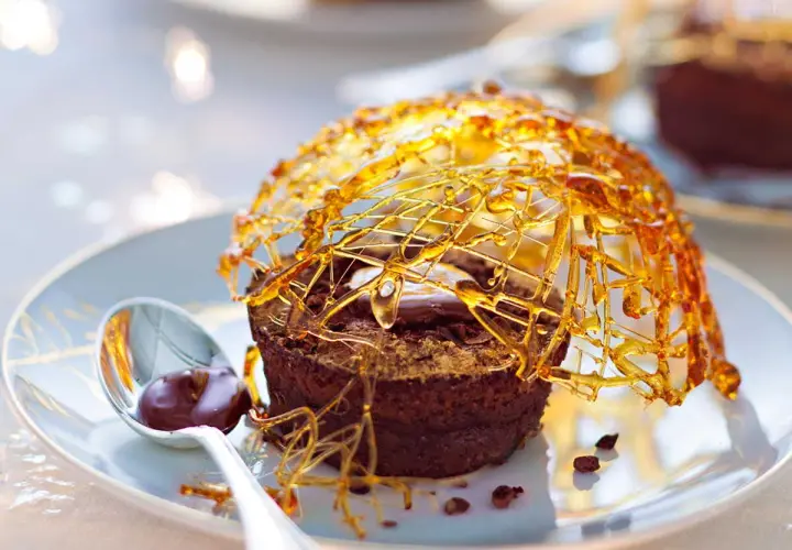 Gâteau au chocolat surmonté d'une décoration caramel facile et aérienne, avec une cuillère de sauce au chocolat.