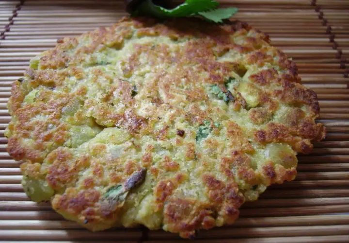 Une galette de pois cassés dorée et croustillante, garnie de persil frais, repose sur un tapis de bambou.