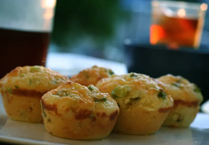 Cinq muffins salés dorés, garnis de fromage et d'herbes, sur une assiette blanche.