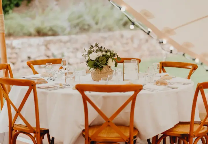 Table dressée pour un repas traditionnel mariage français, avec des chaises en bois, des fleurs et des petits pains.