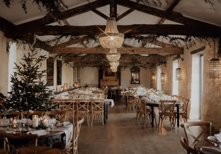 Une salle de réception décorée pour un mariage en hiver, avec un sapin illuminé, des guirlandes lumineuses et des tables dressées.